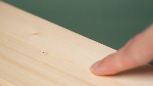 橄欖綠背景，一片塗裝木器還原漆WOODLIKE的實木木板，一根手指滑過木頭的塗膜平滑表面。
