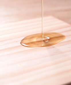 臘感護膜FINISH自上而下澆淋在木桌上放置的松木木板。質感細緻的金黃色透明塗料塗裝在木板表面，木紋仍清晰可見。