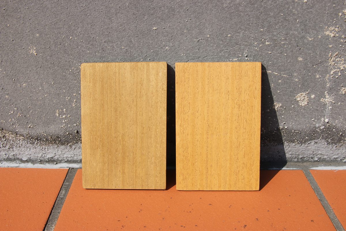 兩片顏色相同的木板倚靠水泥牆邊立起，放置在戶外的陽光下